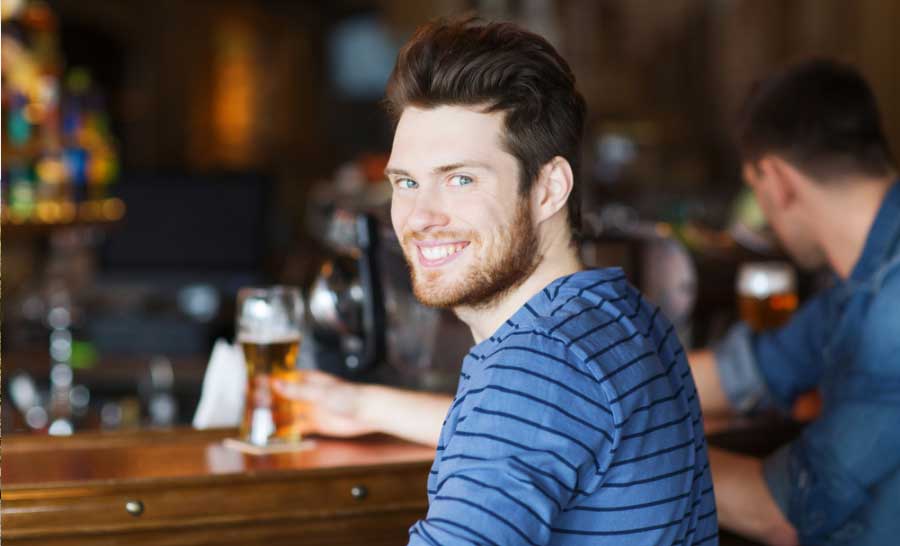 Jünger Engländer sitzt mit einem Pint an der Bar eines typisch englischen Pubs